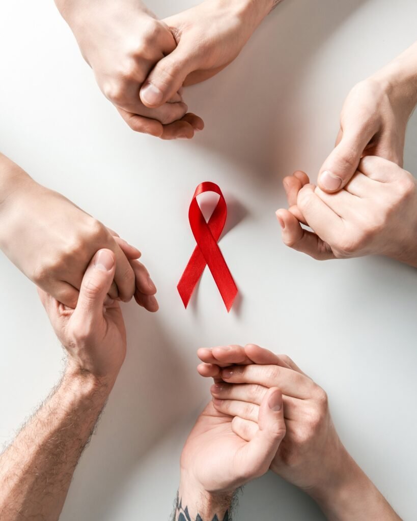 top view of people holding hands and aids awareness red ribbon on white background